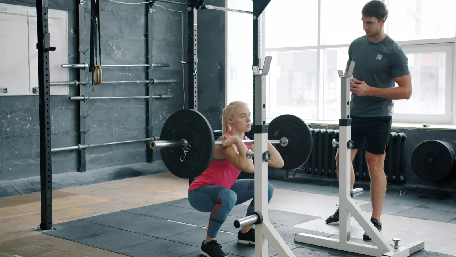 A trainer coaching a member through a barbell front squat